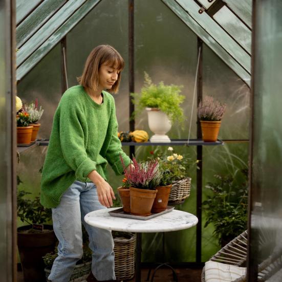 Kvinde, der placerer to potteplanter på et bord i et drivhus.