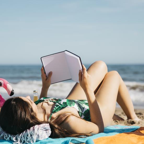 Kvinde, der ligger på stranden og læser en bog.