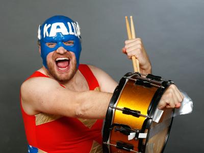 En mand i rød dragt og blå maske spiller trommer og ser vild ud. 