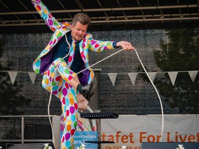 En mand i farverigt jakkesæt optræder på en scene. 