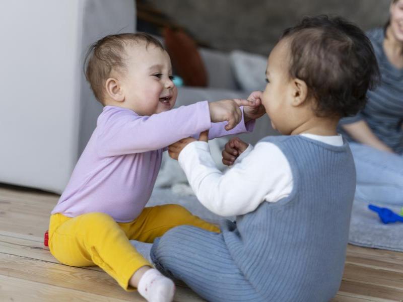 To babyer sidder på gulvet. De leger og griner. 