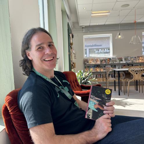 Kenneth sidder i en rød lænestol og viser bogen "Affæren med den tabte tids luner" frem.